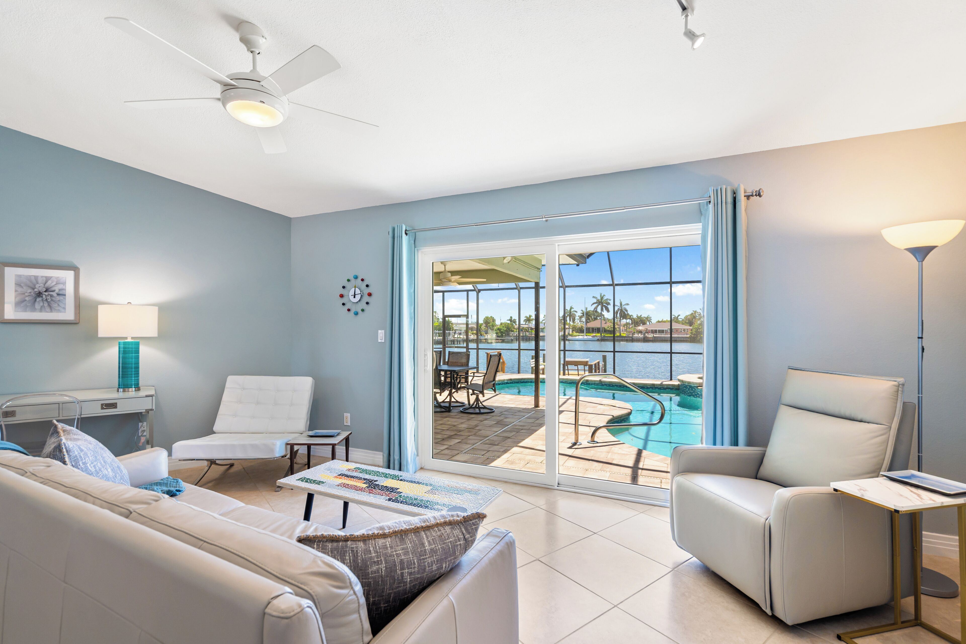 A modern living room with a pool view, a ceiling fan, and a dining area.