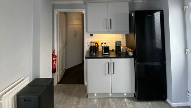 A compact kitchen with white cabinets, a black refrigerator, and a wooden floor. - House Sleeps 4- Free Parking, Garden, Pet Friendly (Bournemouth)