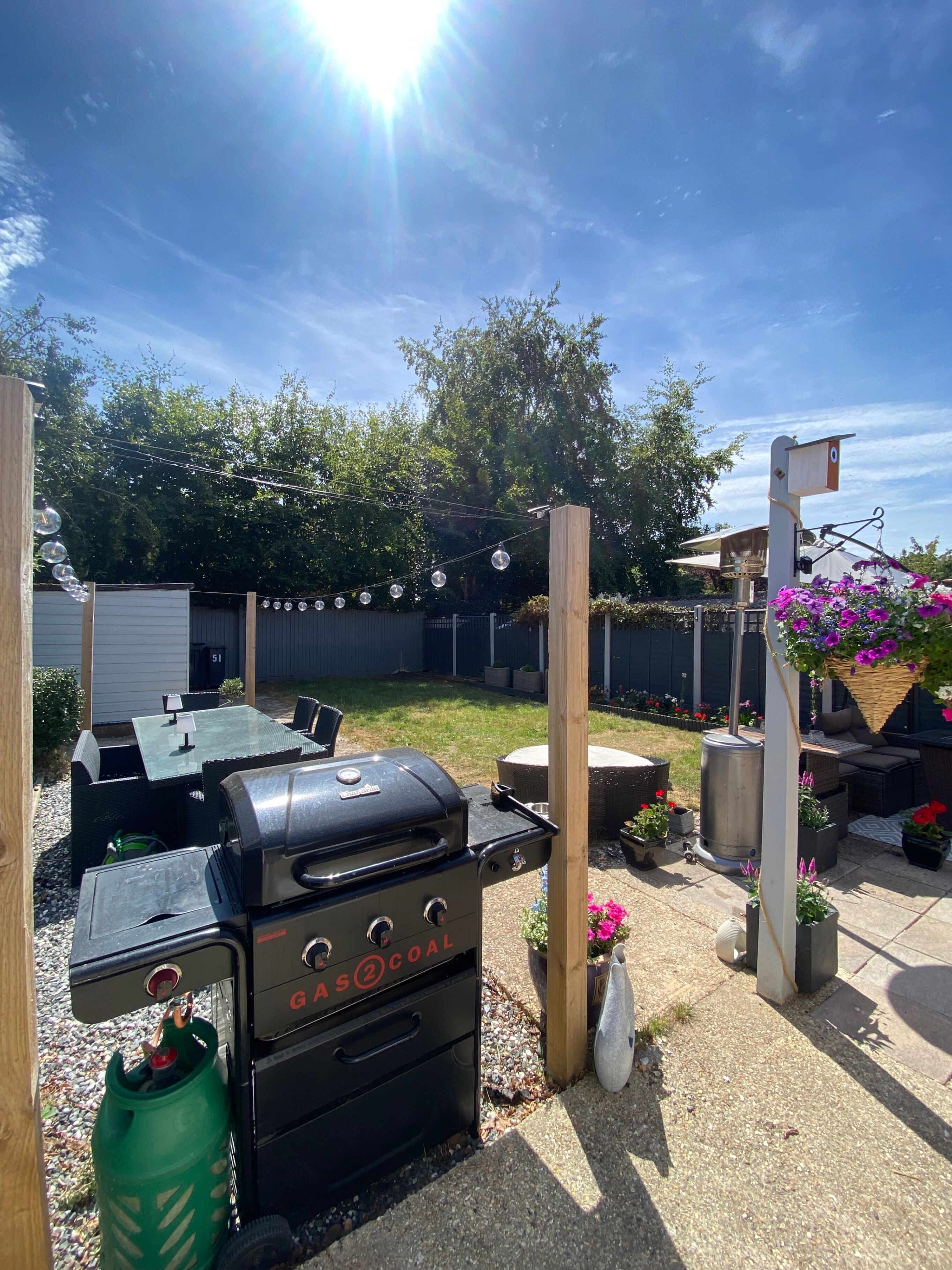Un jardin avec un barbecue, du mobilier d’extérieur et une pergola ornée de plantes en suspension.
