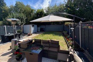 Ein Garten mit Terrasse, Gartenmöbeln, Grill und einer überdachten Sitzgelegenheit.