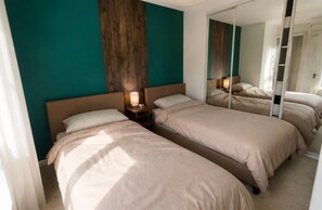 Une chambre d’hôtel avec deux lits, un mur décoratif en bois et un miroir qui reflète la pièce.