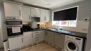 A modern kitchen with built-in appliances, a washing machine, and a window with a view. - House Sleeps 4- Free Parking, Garden, Pet Friendly (Bournemouth)