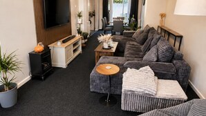 A modern living room with a large flat-screen TV, a sofa set, a coffee table, and a dining area with chairs. - House Sleeps 4- Free Parking, Garden, Pet Friendly (Bournemouth)