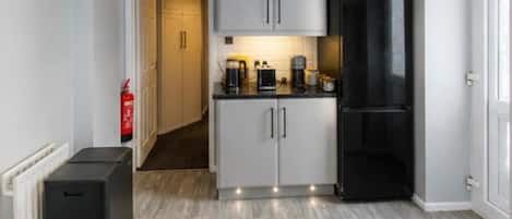 A compact kitchen with white cabinets, a black refrigerator, and a coffee maker on the counter.