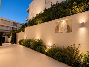 A modern building with a flat facade, a narrow pathway, and a wall-mounted light fixture. - ELAIA Luxury Voula Residence with Private Pool on Athens Riviera (Voula)