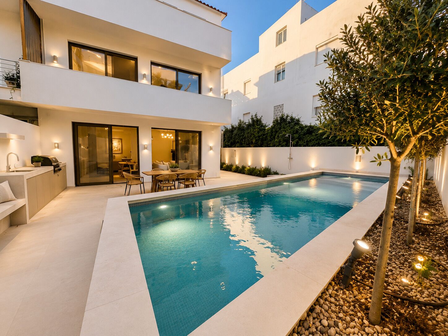 A modern two-story house with a swimming pool, outdoor seating, and a well-lit patio area.