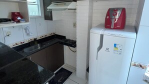 A compact kitchen with white cabinets, a black countertop, a red coffee maker, and a white refrigerator. - BEST VIEW OF BICA BEACH (Rio de Janeiro)