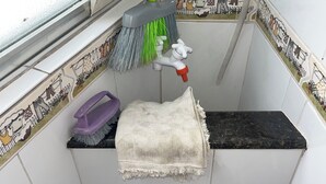 A bathroom corner with a towel hanging on a rack, a purple cleaning brush, a red bucket, and a mop with green bristles. - BEST VIEW OF BICA BEACH (Rio de Janeiro)