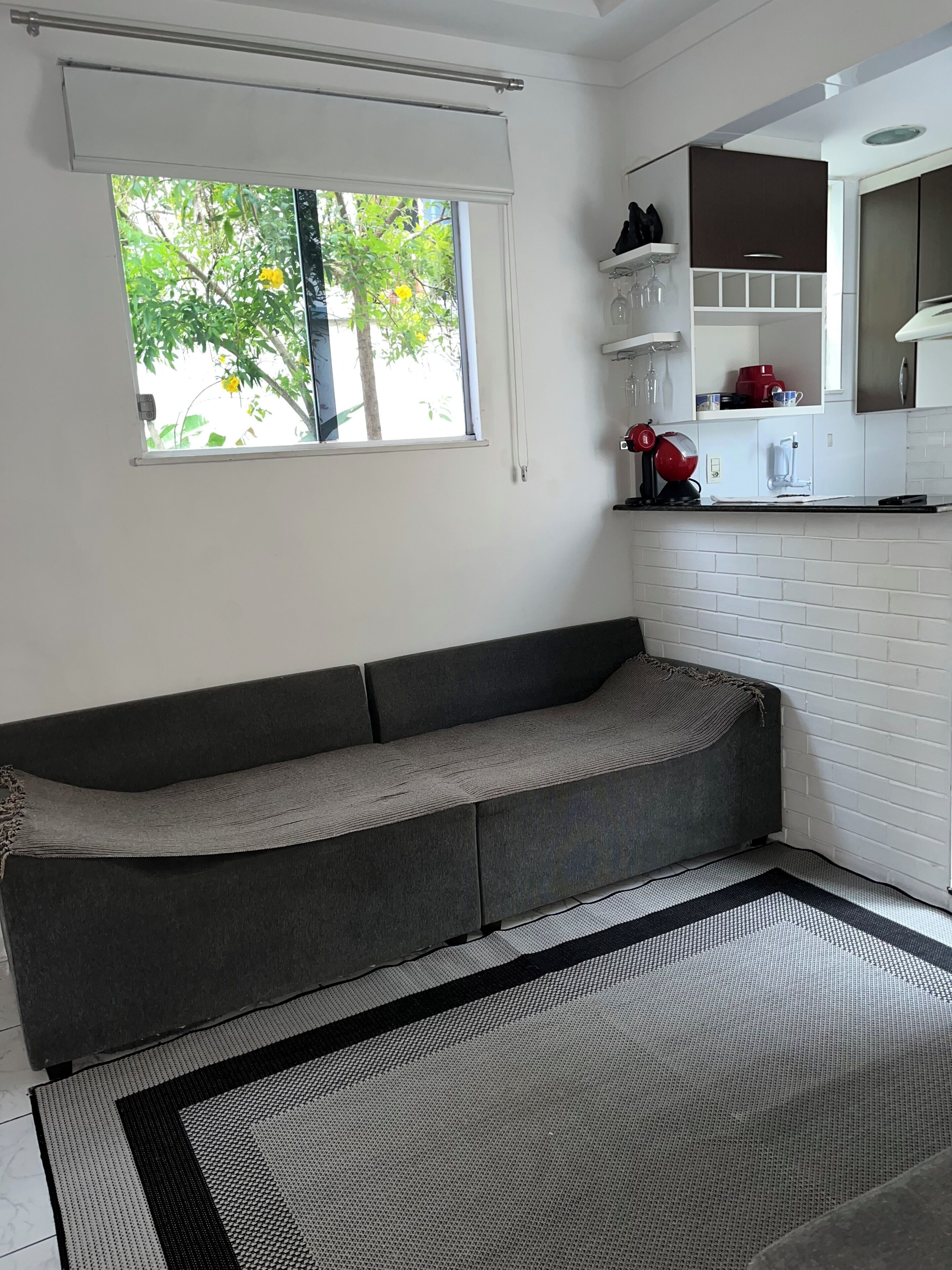 A modern living room with a grey sofa, a patterned rug, and a kitchen area with white cabinets and a red appliance.