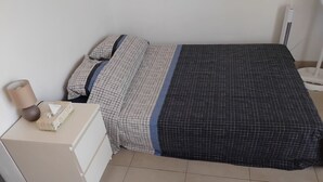 A bed with a patterned bedspread, a bedside table with a lamp, and a white dresser. - Detached studio apartment across from Riquier Station, with a beautiful view of the hills of Nice (Nice)