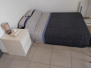 Ein Bett mit einem gemusterten Überwurf, ein Nachttisch mit einer Lampe und eine weiße Kommode.