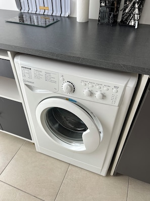 A front-loading washing machine with control panel, located in a kitchen area with a countertop above. - Detached studio apartment across from Riquier Station, with a beautiful view of the hills of Nice (Nice)