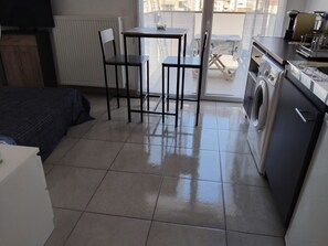 A compact room with a bed, a table with chairs, a washing machine, and a radiator. - Detached studio apartment across from Riquier Station, with a beautiful view of the hills of Nice (Nice)