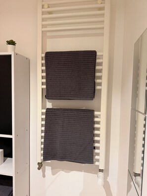Ein Badezimmer mit einem weißen Handtuchhalter, der zwei Handtücher, eine kleine Topfpflanze und einen Spiegel trägt.