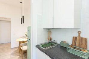 A modern kitchen with white cabinets, a green countertop, and a dining area with a table and chairs. - The Golden Rooster -1 min to the station (Roma)