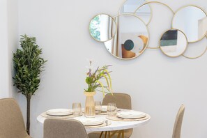 A dining area with a round table set for four, surrounded by chairs. There is a potted plant to the left and a wall-mounted mirror above the table. - The Golden Rooster -1 min to the station (Roma)
