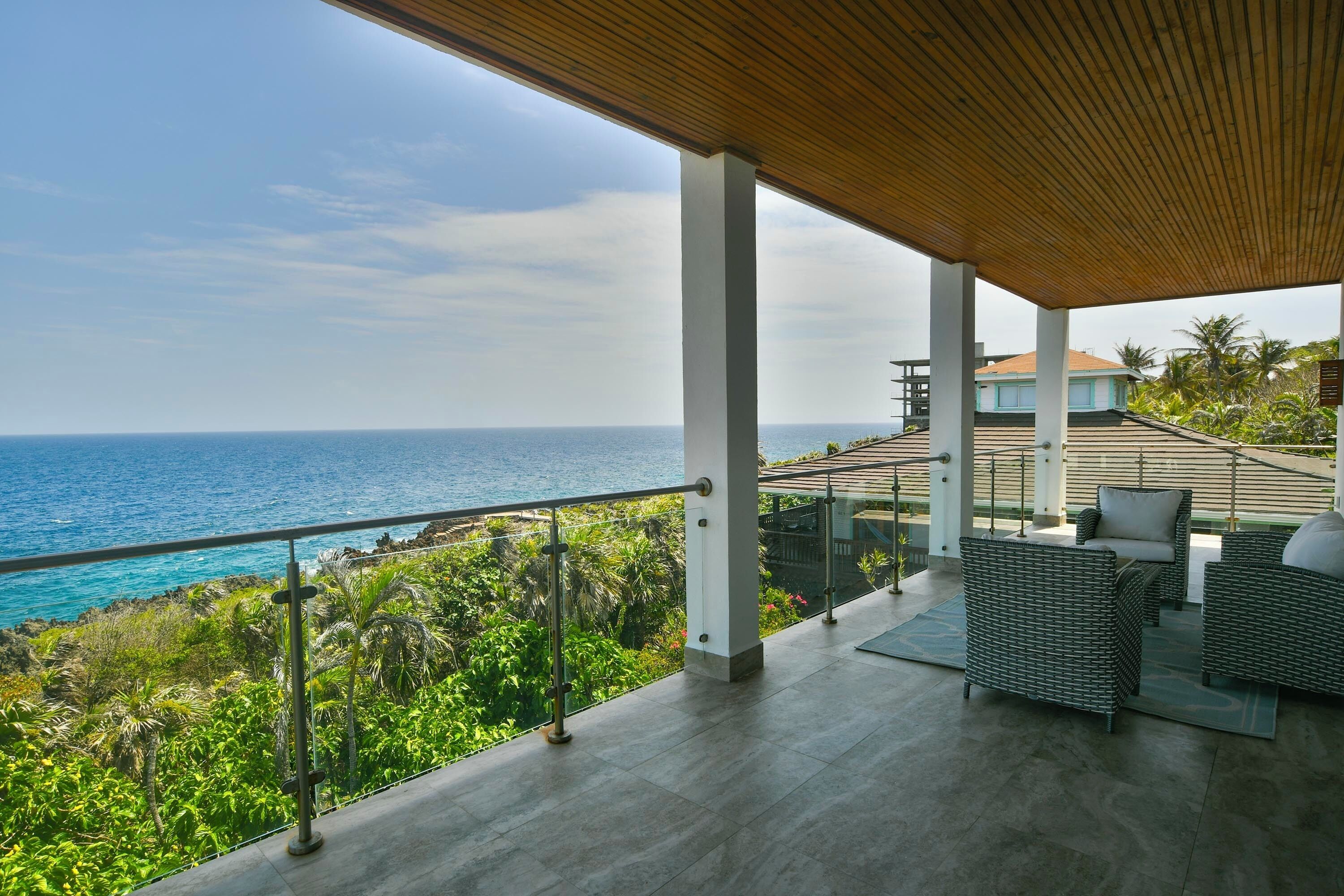 A covered outdoor area with a view of the ocean, featuring a seating area with cushions and a railing.