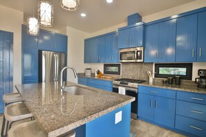 Eine moderne Küche mit blauen Schränken, Edelstahlgeräten, Granit Arbeitsplatten und Pendelleuchten.