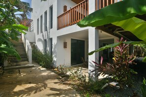 Ein modernes Gebäude mit weißer Fassade, einem Holzbalkon und einem Gartenbereich mit verschiedenen Pflanzen sowie einer Treppe zum Eingang.