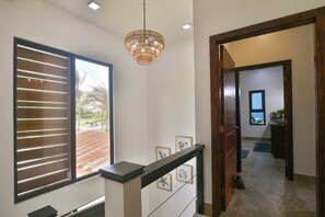 A hallway with a wooden door, a staircase, and a view of a garden through a window with blinds. - Casa Tranquilidad 3-bed by Island House Vacation Rentals (West Bay)