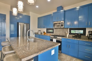 A modern kitchen with blue cabinets, stainless steel appliances, granite countertops, and pendant lighting. - Casa Tranquilidad 3-bed by Island House Vacation Rentals (West Bay)
