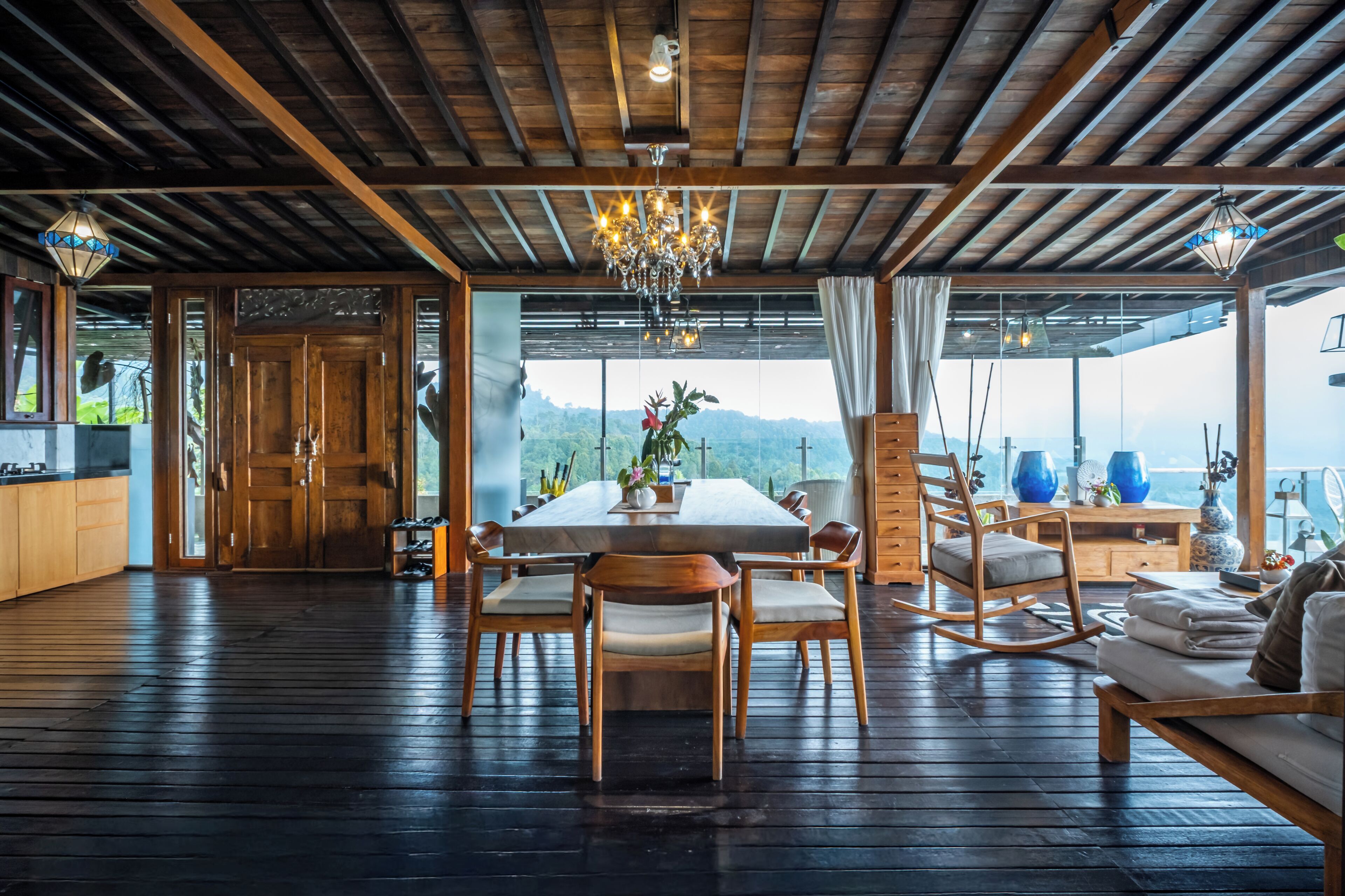 A spacious dining area with a wooden table and chairs, a chandelier, and a view of the mountains through large windows.