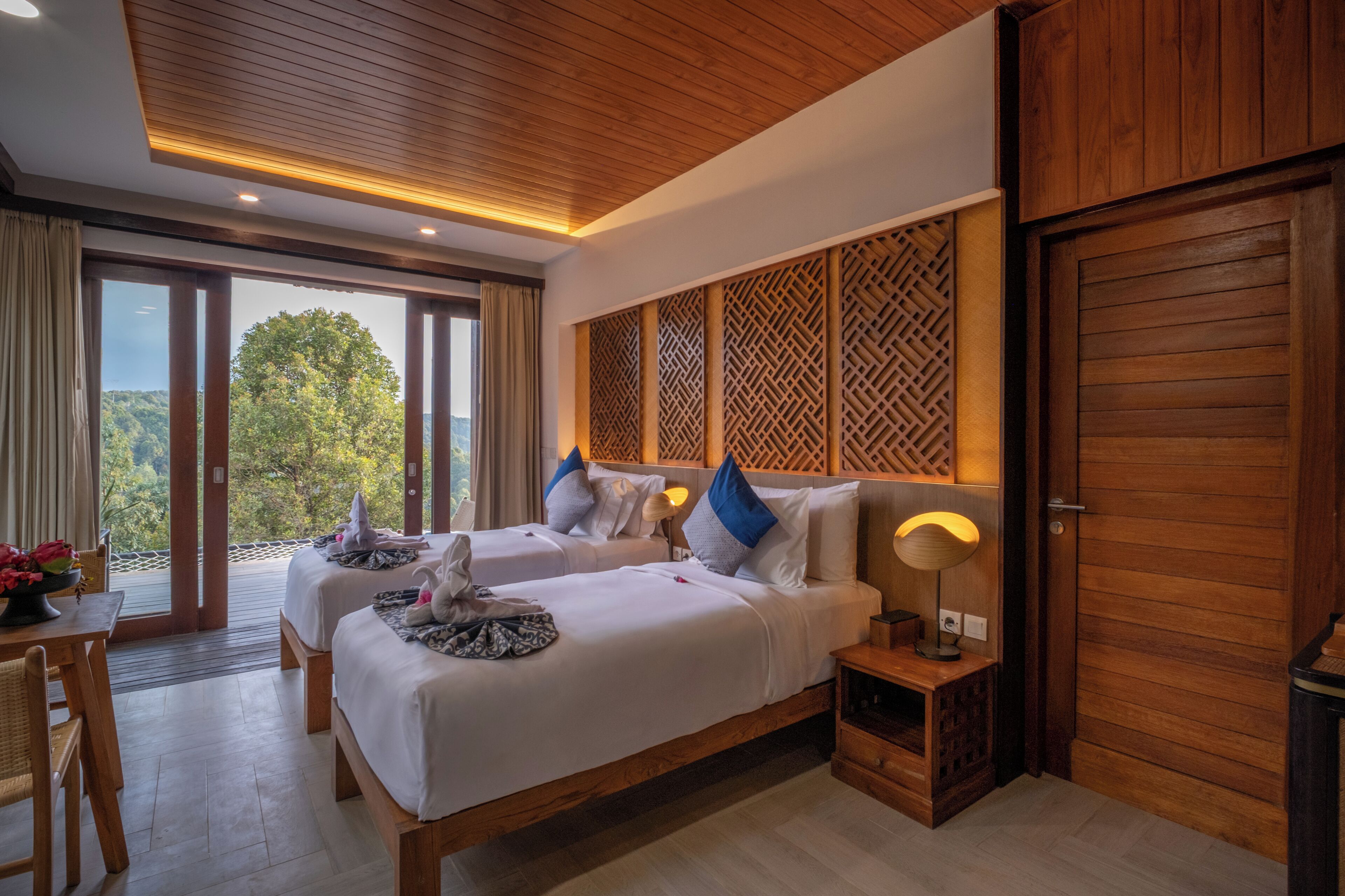 Habitación de hotel con dos camas, techo de madera, vistas a la vegetación y una puerta.