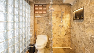 A bathroom with a glass shower enclosure, a toilet, and a marble-tiled wall.