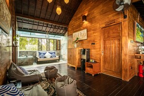 A cozy interior with a wooden ceiling, a sofa with patterned cushions, a coffee table, and a decorative wall piece. - Munduk Harvest Palace (Munduk)