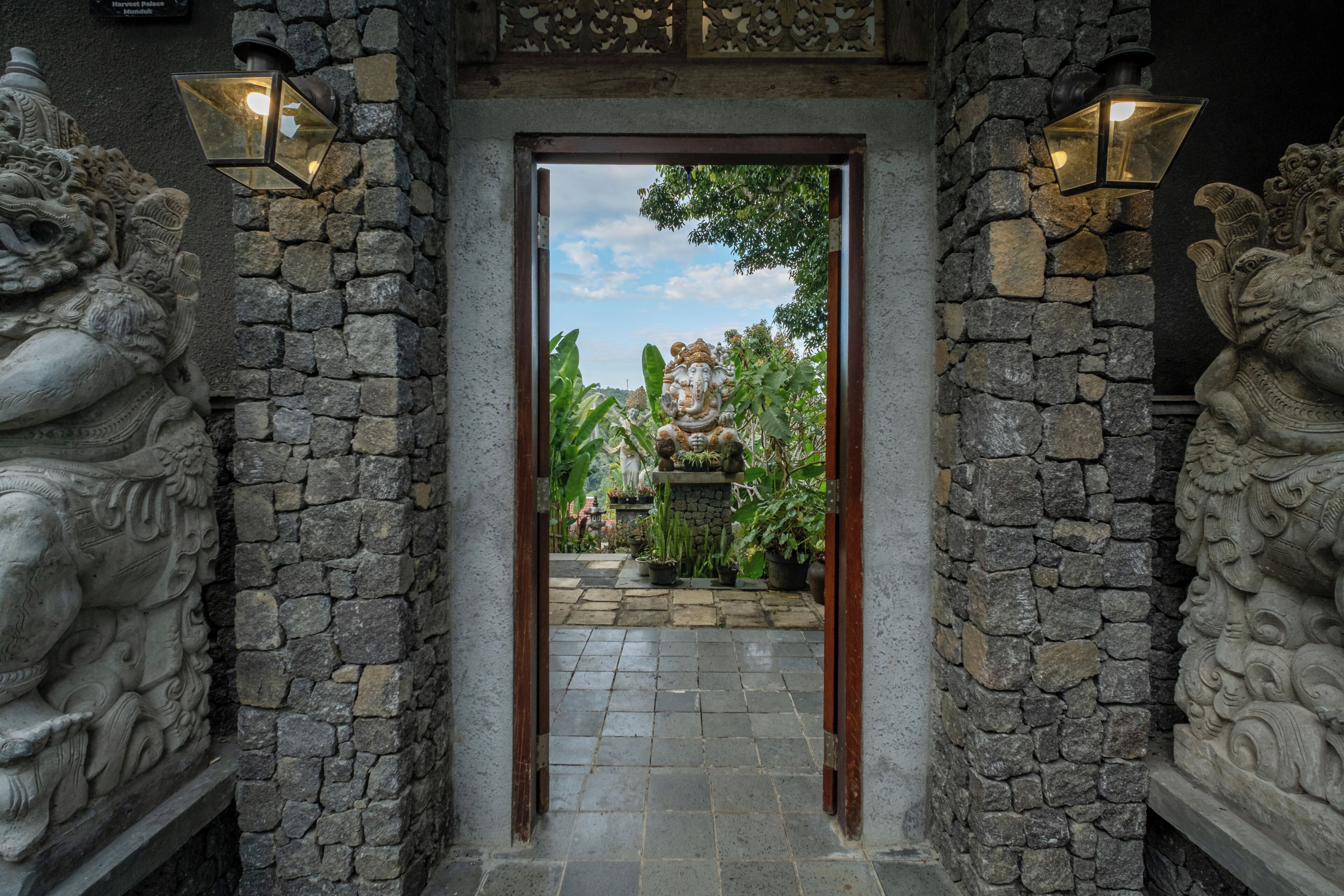 A stone entrance with a statue and a view of a garden.