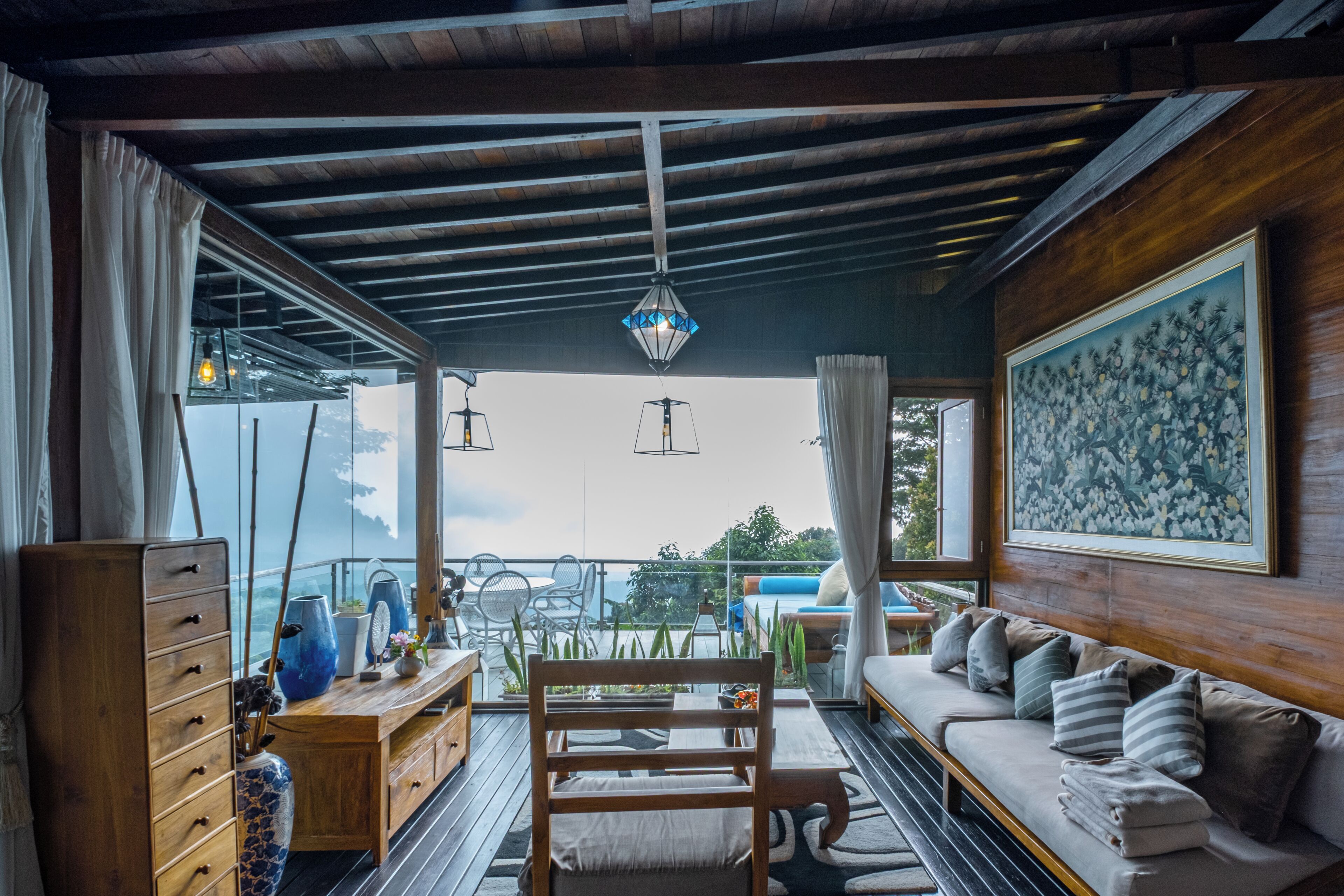 Una habitación amplia con techo de madera, un ventanal grande, un sofá, una mesa de comedor y un cuadro en la pared.