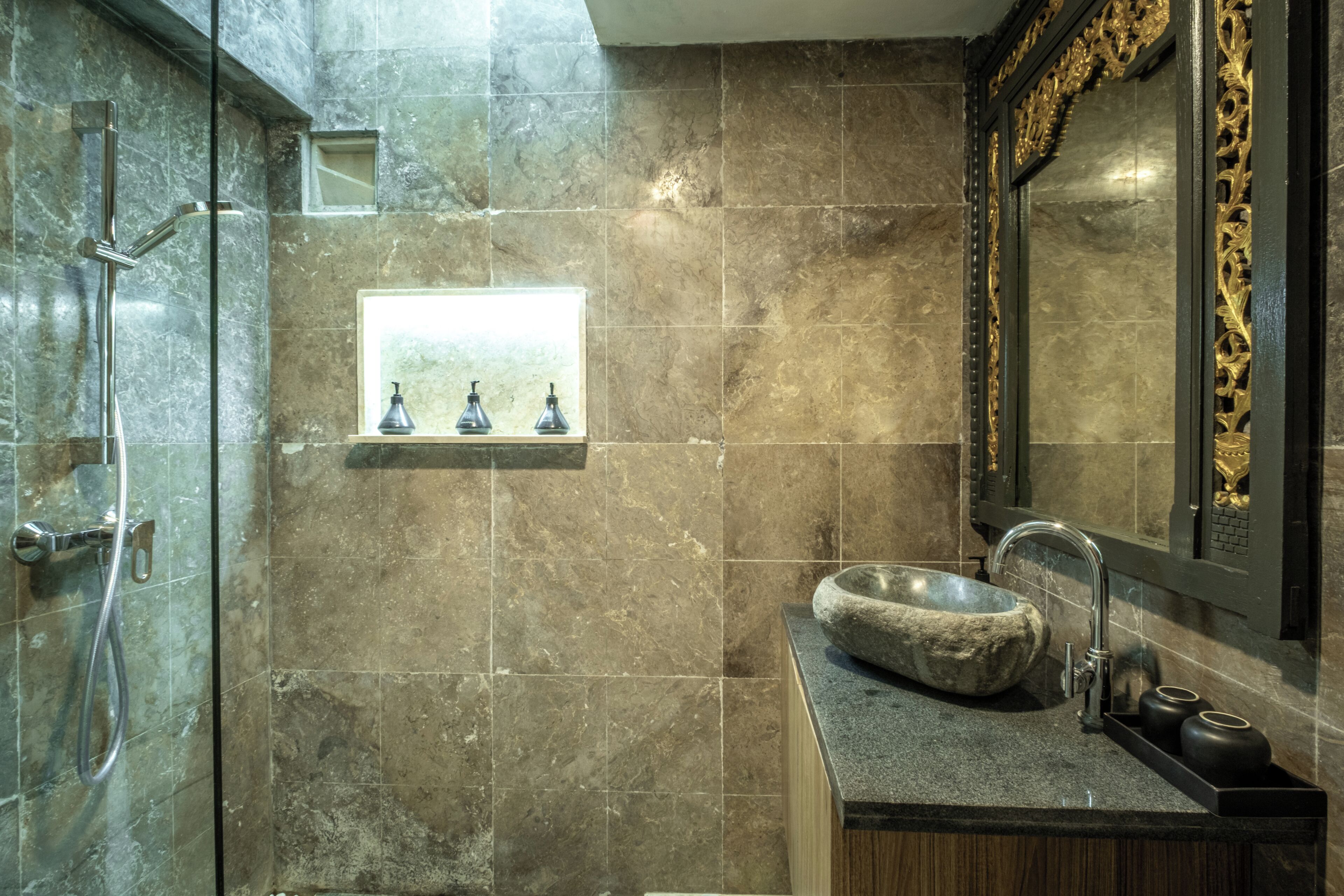 A bathroom with a stone sink, a mirror with ornate frame, and a shower area.