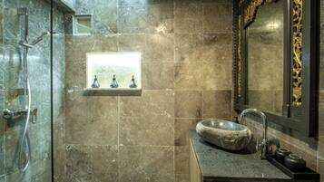 A bathroom with a stone sink, a mirror with ornate frame, and a shower area.