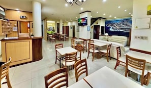 A hotel lobby with a reception desk, dining area with tables and chairs, a sofa, and a large mural on the wall. - Hotel Marbella (Punta del Este)