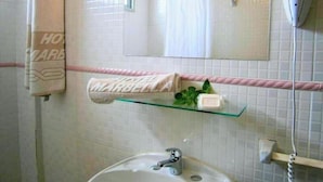 Un baño con lavamanos, espejo, toallero y repisa de vidrio con artículos de aseo.