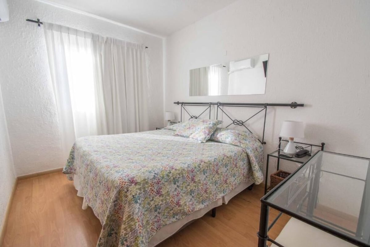 A bedroom with a bed, a bedside table, a mirror, and a window with curtains.