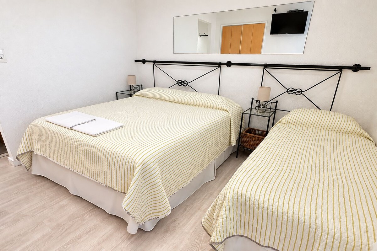 Una habitación doble con dos camas, una mesita de noche, una lámpara y un espejo en la pared.