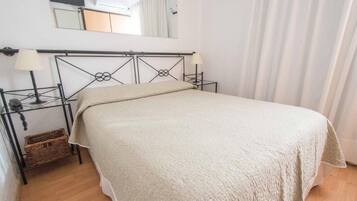 A single bed with a headboard, bedside lamps, a small wicker basket, and a mirror on the wall.