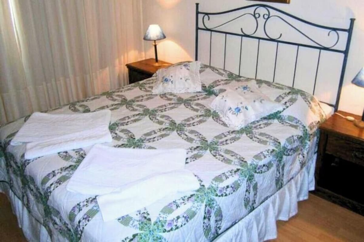 A neatly made bed with a patterned bedspread and pillows, two bedside lamps, and a bedside telephone.