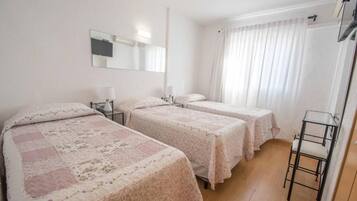 Habitación de hotel con dos camas, un espejo, una mesita de noche con lámpara y una ventana con cortinas.