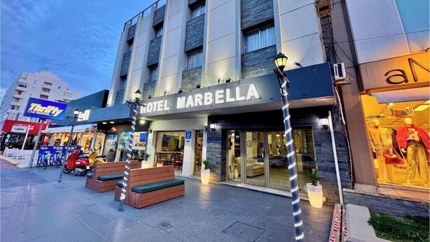 Un hotel llamado 'HOTEL MARBELLA' con una fachada moderna, mobiliario exterior y una entrada visible.