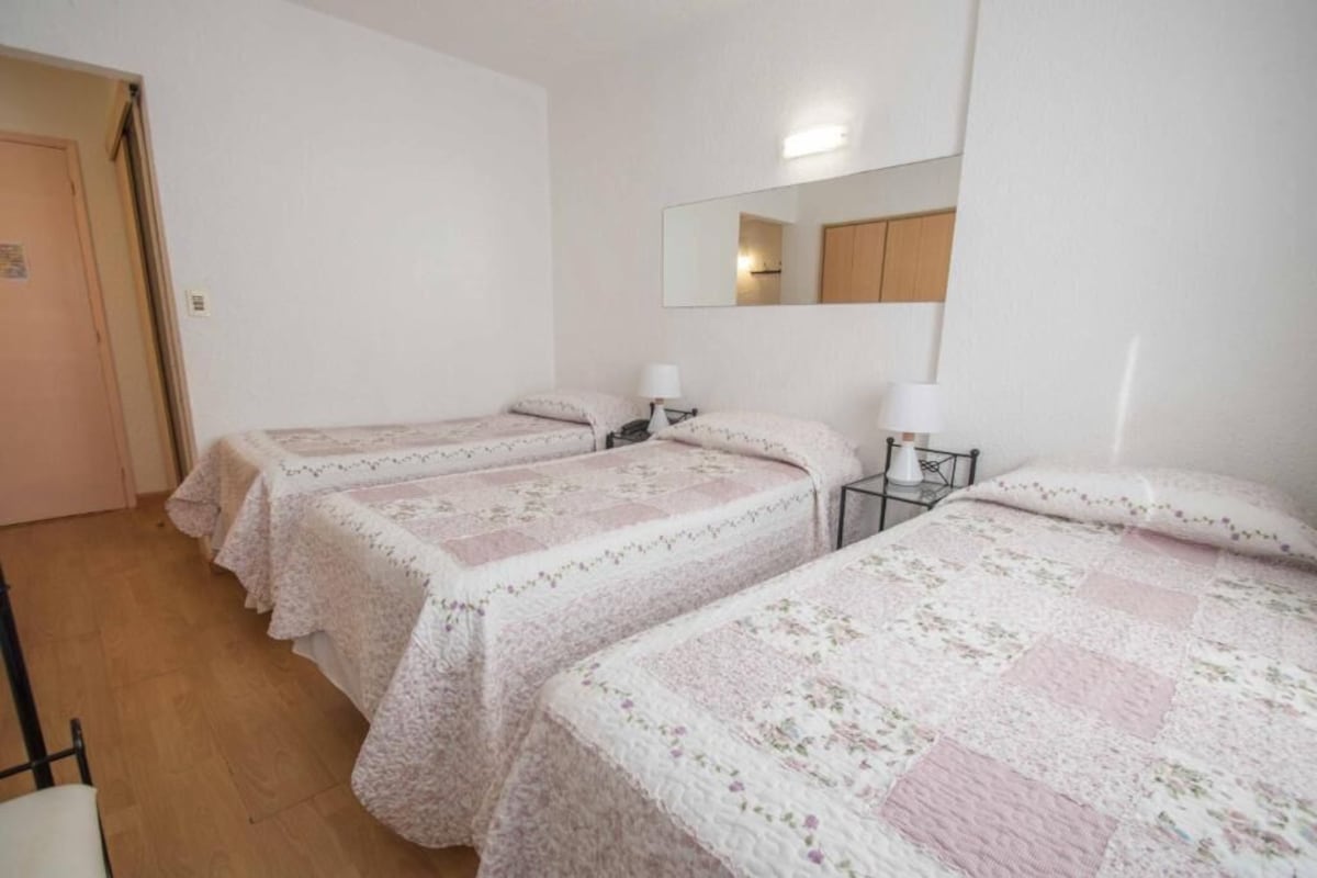 A room with two single beds, a bedside table with a lamp, a mirror on the wall, and a door.