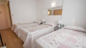 A room with two single beds, a bedside table with a lamp, a mirror on the wall, and a door.