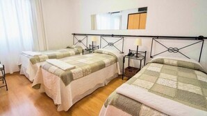 Habitación de hotel con tres camas, suelo de madera y un espejo en la pared.