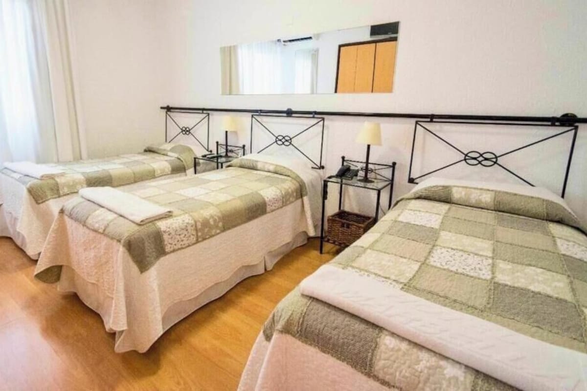 A hotel room with three beds, a wooden floor, and a mirror on the wall.