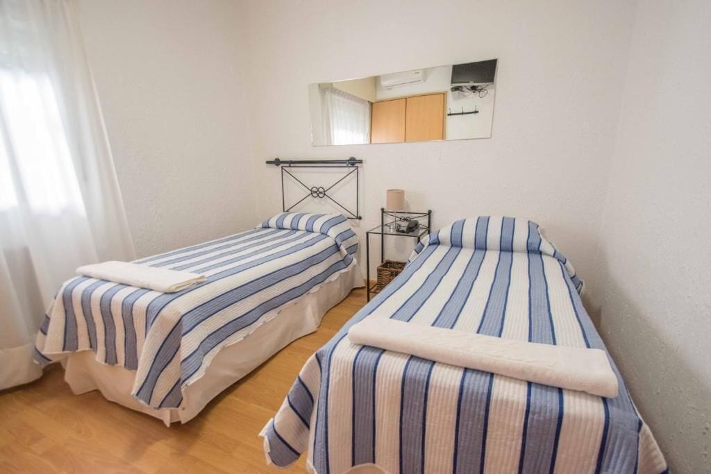 Una habitación con dos camas individuales, una mesita de noche con lámpara y un espejo en la pared.