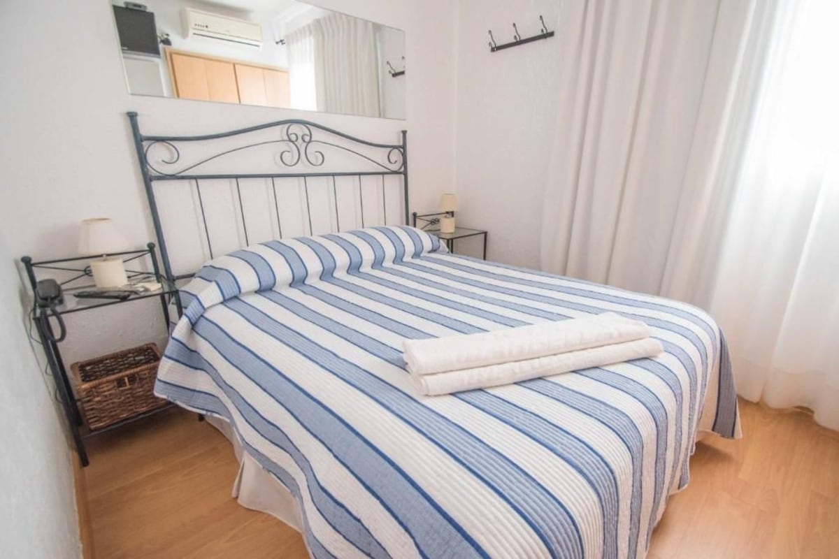 A bed with a striped bedspread, a bedside table with a lamp, and a small wicker basket.