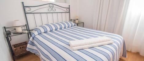 A bed with a striped bedspread, a bedside table with a lamp, and a small wicker basket.
