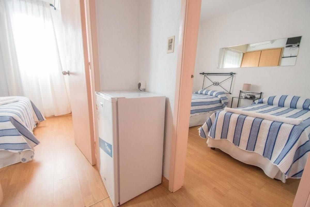 A hotel room with a bed, a desk, a chair, a mirror, and a window with curtains.