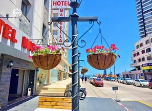 A street view with a hotel sign, hanging flower baskets, and parked cars. - Hotel Marbella (Punta del Este)